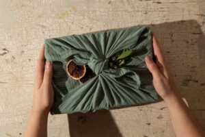 Hands holding a pack covered in green cloth with leaves, flowers and soil